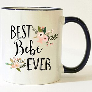 May include: White ceramic mug with a black rim and handle. The mug has a floral design and the text "BEST Bebe EVER" in black.