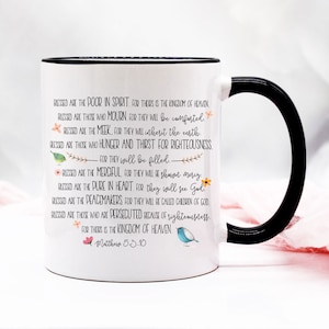 May include: White ceramic mug with a black handle. The mug features a black rim and a quote from the Bible, Matthew 5:3-10, in black text. The quote reads: "Blessed are the poor in spirit, for theirs is the kingdom of heaven. Blessed are those who mourn, for they will be comforted. Blessed are the meek, for they will inherit the earth. Blessed are those who hunger and thirst for righteousness, for they will be filled. Blessed are the merciful, for they will be shown mercy. Blessed are the pure in heart, for they will see God. Blessed are the peacemakers, for they will be called children of God. Blessed are those who are persecuted because of righteousness, for theirs is the kingdom of heaven. Matthew 5:3-10."