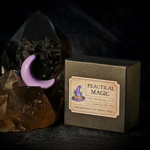 May include: A dark brown box with a label that reads "Practical Magic" next to a purple crescent moon and a large dark crystal. The label features a witch's hat illustration and ingredient list. The box is handpoured with Moon Wax.