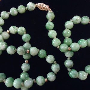 May include: A green jade bead necklace with gold accents. The necklace is made of round beads that are strung together with a gold clasp.