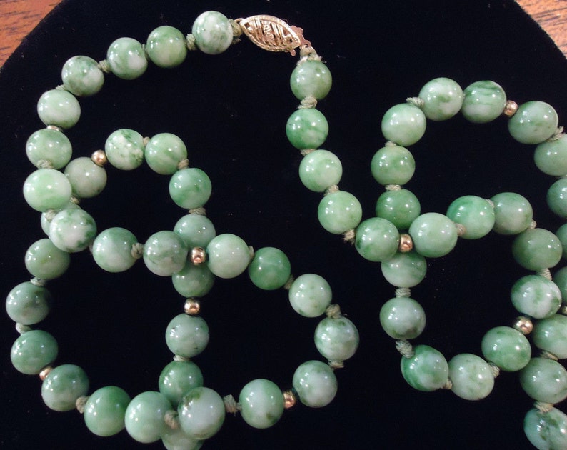 May include: A green jade bead necklace with gold accents. The necklace is made of round beads that are strung together with a gold clasp.