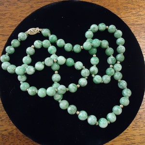 May include: A green jade bead necklace with a gold clasp. The beads are round and have a marbled pattern.