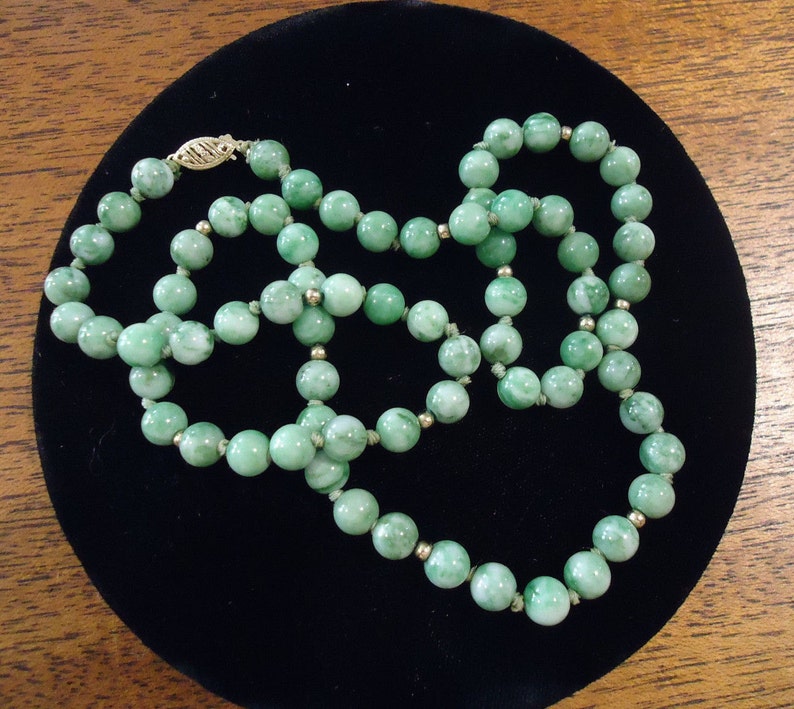 May include: A green jade bead necklace with a gold clasp. The beads are round and have a marbled pattern.