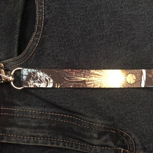 May include: A black and white printed lanyard with a silver key chain. The lanyard features a graphic of a clock face with a maze pattern.