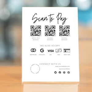 May include: White sign with the text "Scan to Pay" at the top.  Three QR codes are displayed below the text, labeled "Apple Pay", "Venmo", and "Paypal".  Below the QR codes, the sign reads "We Also Accept" and displays icons for Mastercard, Google Pay, Visa, Cash, and Credit Card.  The bottom of the sign reads "Connect With Us" and includes a website address and social media icons for Twitter, Facebook, Instagram, and Pinterest.