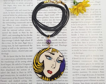 Op de afbeelding: Een zwarte koordsnoer met een ronde hanger met een popart-stijl illustratie van een vrouwengezicht met gele, blauwe en rode kleuren. De hanger is omgeven door een zwart koord.
