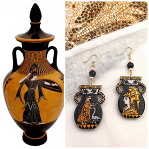 May include: A pair of black and gold earrings shaped like ancient Greek amphorae with black and white painted figures. The earrings are hanging from black beads and gold chains.