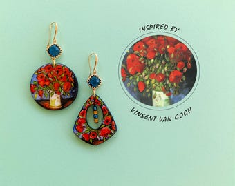 May include: A pair of gold earrings with blue gemstone accents. Each earring features a round or teardrop-shaped pendant with a painted image of red poppies in a vase, inspired by Vincent van Gogh.