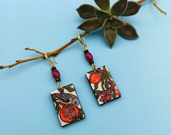 May include: A pair of gold earrings with red and black beads and rectangular pendants featuring a bird and pomegranate design.