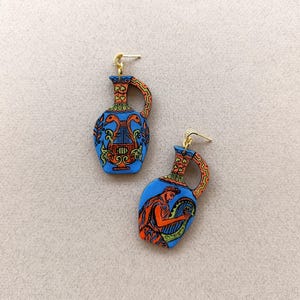 May include: A pair of blue and orange ceramic earrings shaped like ancient Greek amphorae. One earring features a lyre and two birds, while the other features a man playing a lyre.