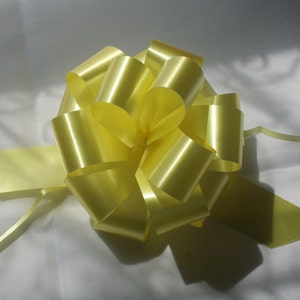 Może przedstawiać: Duża, żółta kokarda z satyny z zakręconym końcem wstążki. Kokarda jest zawiązana w klasycznym, symetrycznym kształcie.