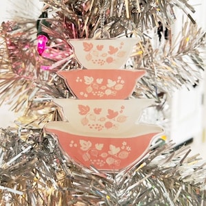 May include: A pink and white Christmas ornament shaped like a stack of three nesting bowls with a floral pattern.