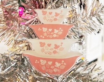 May include: A pink and white Christmas ornament shaped like a stack of three nesting bowls with a floral pattern.