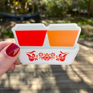 May include: A white ceramic butter dish with two red and orange butter containers. The dish has a floral and bird design in red and orange.