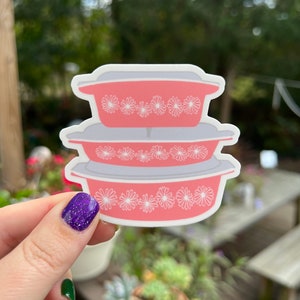 May include: A sticker of three pink and white casserole dishes stacked on top of each other. The dishes have a floral pattern around the rim.