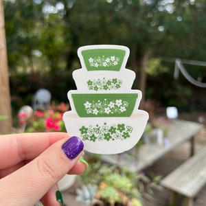 May include: A set of three green and white nesting bowls with a floral pattern. The bowls are stacked on top of each other.
