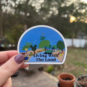 May include: A blue and green sticker with a cartoon illustration of a greenhouse and the text "Living With The Land".