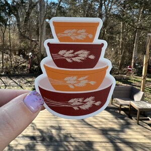 May include: A sticker of a stack of four vintage mixing bowls with a wheat design. The bowls are orange, brown, and red.