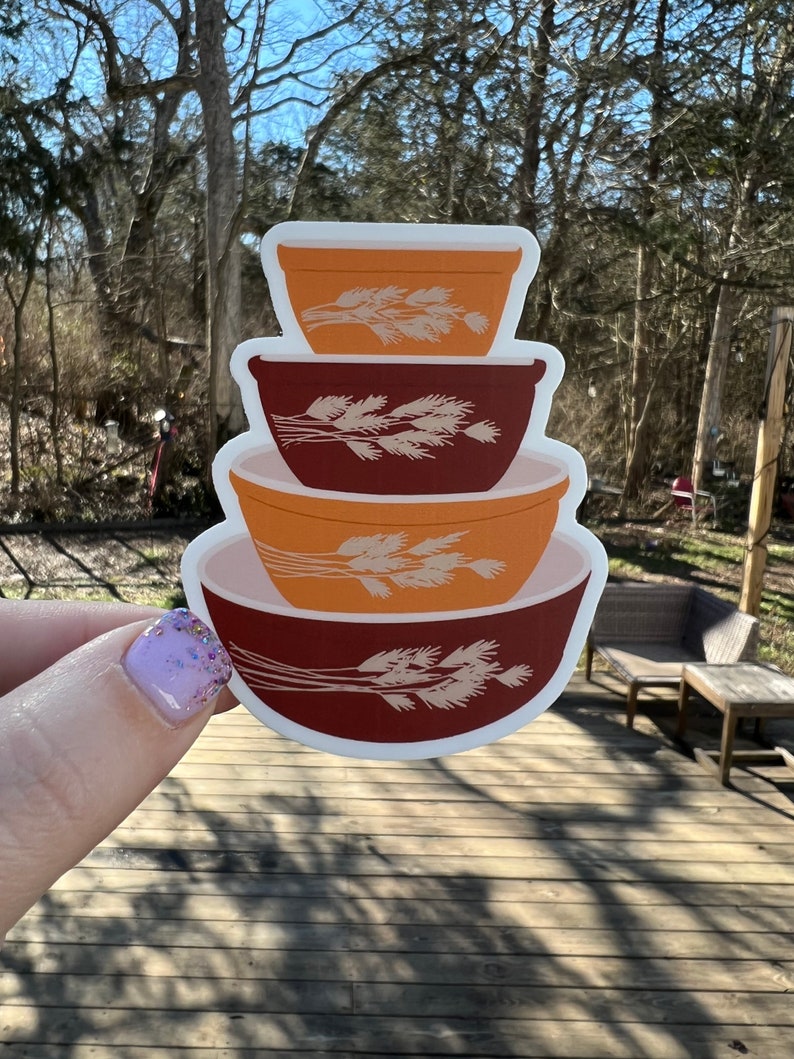 May include: A sticker of a stack of four vintage mixing bowls with a wheat design. The bowls are orange, brown, and red.