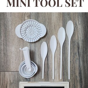May include: White sensory tools for children, including a colander, measuring cups, and spoons. The tools are arranged on a wooden surface with a sign that reads "MINI SET".