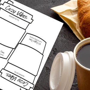 May include: A coffee-themed image featuring a printable cup cozy design with the text "Cozy Vibes" and "It's Coffee Time". A paper coffee cup with a lid and a croissant are also visible. The image is on a dark surface.