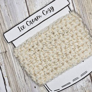 May include: A white crocheted ice cream cozy with gold thread accents. The cozy is on a white background with the words "Ice Cream Cozy" written on it.