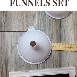 May include: Two white plastic funnels of different sizes, with a wooden ruler measuring 23 cm, and a white wooden sign with black letters that reads "FUNNELS".