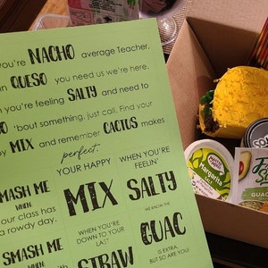 May include: A green and black gift basket with the text "NACHO GIFT BASKET" and "First Day of School Ideas". The basket contains a variety of items, including a yellow and green pinata, a jar of salsa, a jar of guacamole, and a bag of chips.