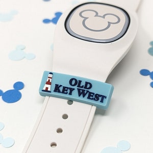 May include: White Disney MagicBand with a blue and white Old Key West charm featuring a lighthouse. The charm is attached to the band with a Mickey Mouse head design.
