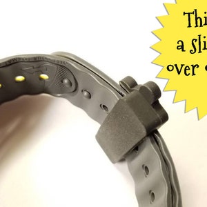 K&ouml;nnte beinhalten: Nahaufnahme eines grauen, verstellbaren Armbands mit einem Schiebermechanismus. Das Band hat gelbe Akzente und ein kleines Logo auf der Innenseite. Der Schieber ist so konzipiert, dass er die Enden des Bandes &uuml;berlappt, um einen sicheren Sitz zu gew&auml;hrleisten.