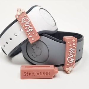 May include: Two pink and white Disney MagicBands with a pink charm that says "Girls Trip" on each. The charm is attached to the band with a gold Mickey Mouse head.