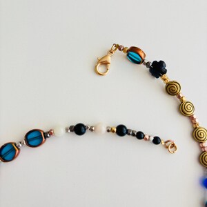 May include: A beaded necklace with a gold clasp and various beads in blue, black, white, and gold. The necklace features oval blue beads, black flower beads, and spiral-shaped gold beads.
