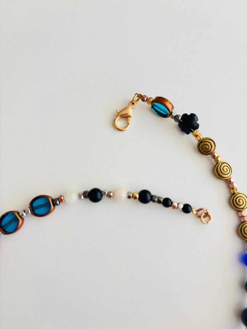May include: A beaded necklace with a gold clasp and various beads in blue, black, white, and gold. The necklace features oval blue beads, black flower beads, and spiral-shaped gold beads.