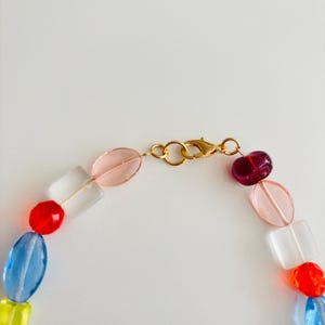 May include: A colorful beaded necklace with a gold clasp. The necklace features a variety of glass beads in shades of red, blue, yellow, pink, and clear. The beads are various shapes, including round, oval, and rectangular.