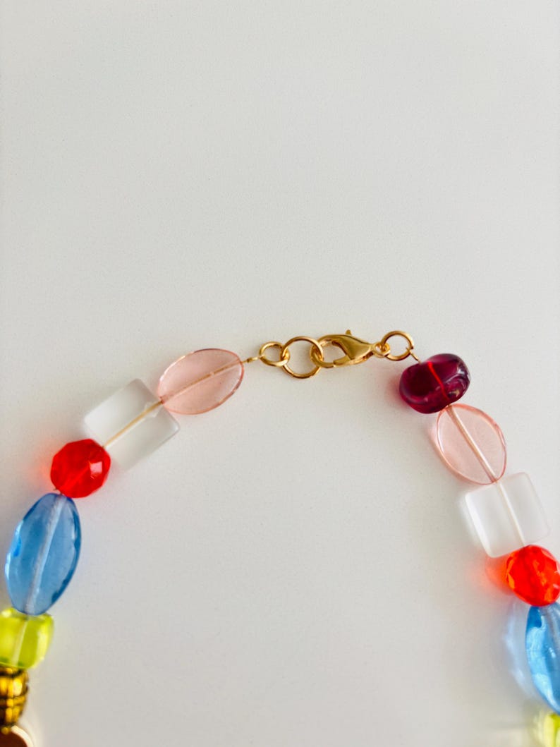 May include: A colorful beaded necklace with a gold clasp. The necklace features a variety of glass beads in shades of red, blue, yellow, pink, and clear. The beads are various shapes, including round, oval, and rectangular.