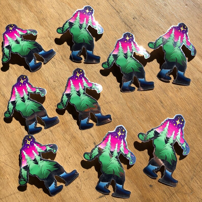 May include: Nine colorful stickers of a Bigfoot with a forest scene inside its head. The stickers are holographic and have a shiny finish. The Bigfoot is green, pink, and blue with a star in the sky.