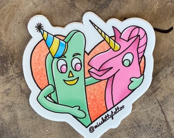 May include: A green stick figure wearing a party hat hugs a pink unicorn with a gold horn. The figures are inside a heart shape with an orange and white background. The text "@misskittytattoo" is at the bottom of the image.
