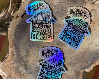 May include: Three iridescent holographic stickers with a house shape and the text "Blow up your TV, Throw away your papers, Move to the country, Build a little home".