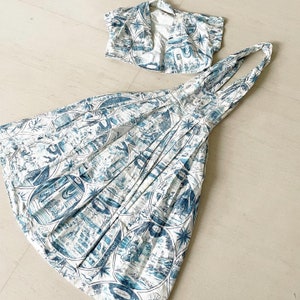 May include: A white and blue patterned dress with a matching cropped top. The dress has a halter neckline and a pleated skirt. The top has a scoop neckline and short sleeves.
