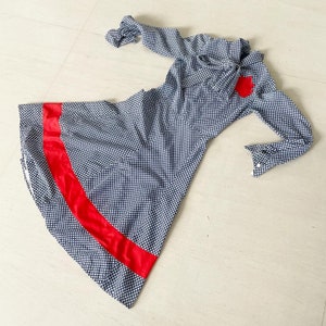 May include: A black and white gingham dress with a red ribbon trim. The dress has long sleeves and a bow at the neck.
