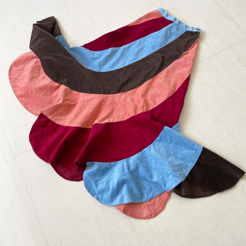May include: A multi-colored skirt with a brown, pink, blue, and burgundy color scheme. The skirt is made of a soft, velvety fabric and has a flowing, layered design.