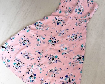 Könnte beinhalten: Ein rosafarbenes Maxikleid mit einem Blumendruck mit blauen, grünen und weißen Blumen. Das Kleid hat dünne Träger und einen quadratischen Ausschnitt.