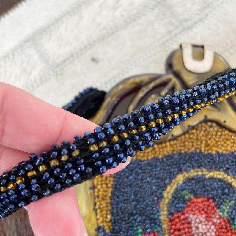 May include: Close-up of a beaded purse strap with alternating dark blue and gold beads. The strap is woven with a black thread.