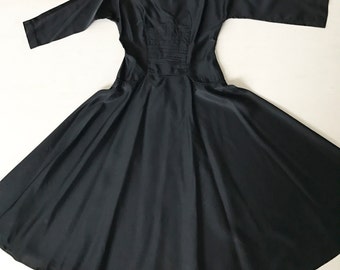 Può includere: Un abito nero con gonna ampia, corpetto aderente e maniche a tre quarti. L'abito ha un design semplice ed elegante.