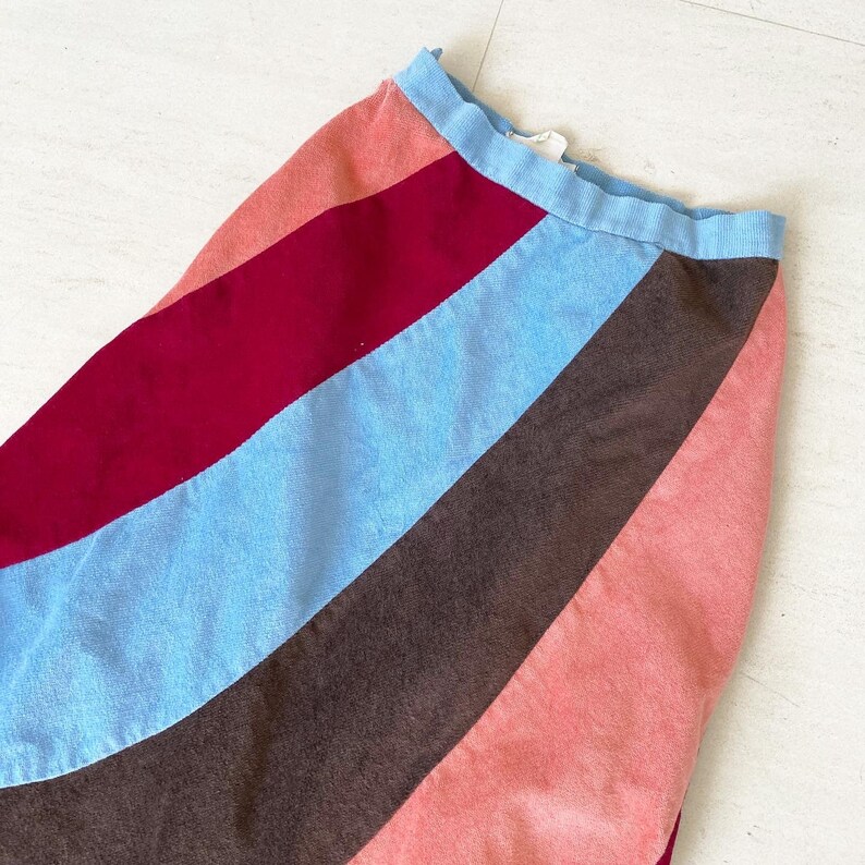 May include: A colorful skirt with diagonal stripes in shades of pink, brown, blue, and burgundy. The skirt has a simple waistband.