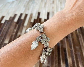 May include: A silver bracelet with multiple crystal embellishments. The bracelet features a cluster of round crystals and teardrop-shaped crystals.