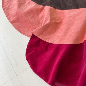May include: A three-tiered skirt with a brown, pink, and burgundy color scheme. The skirt is made of a soft, textured fabric.