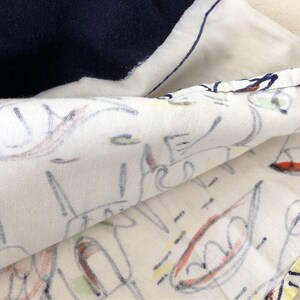 May include: Close-up of a white fabric with a colorful abstract design. The fabric is folded over, revealing a navy blue section underneath.