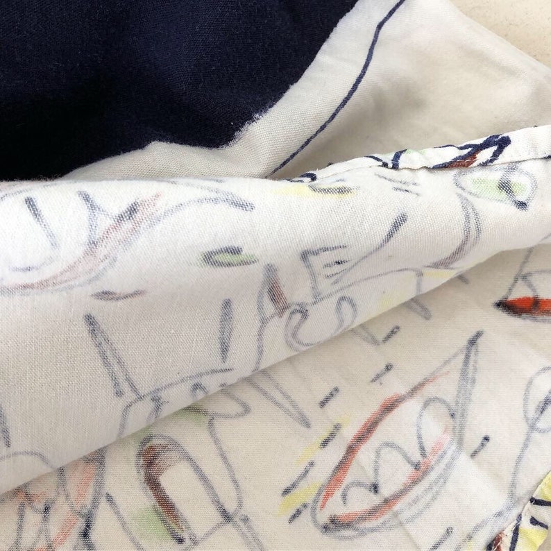 May include: Close-up of a white fabric with a colorful abstract design. The fabric is folded over, revealing a navy blue section underneath.