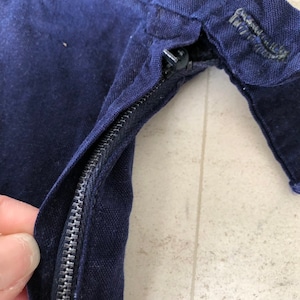 May include: Close-up of a navy blue zipper on a garment. The zipper is metal and has a black pull tab.